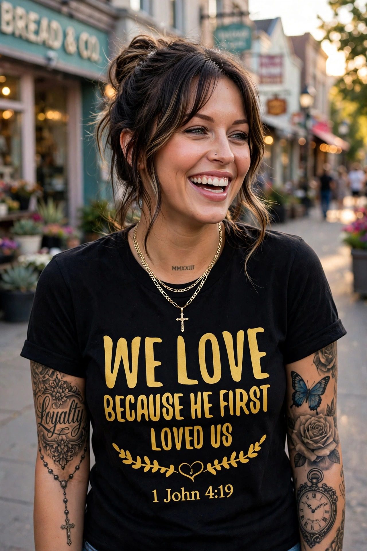 Jelah laughing on a Calgary shopping street, wearing the We Love Because He First Loved Us tee — the words in gold, 1 John 4:19 beneath a laurel wreath and heart